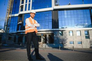 Successful engineer or architect, crane and building construction at backgrpound. Joyous businessman wearing helmet photo