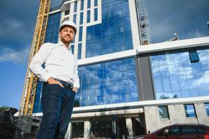 Successful engineer or architect, crane and building construction at backgrpound. Joyous businessman wearing helmet photo