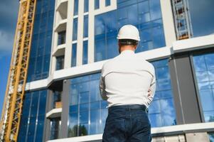 Successful engineer or architect, crane and building construction at backgrpound. Joyous businessman wearing helmet photo