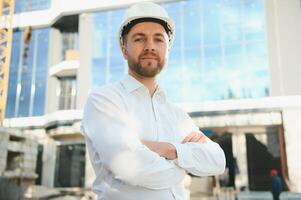 Successful engineer or architect, crane and building construction at backgrpound. Joyous businessman wearing helmet photo