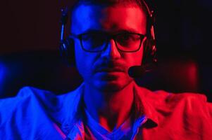Professional Gamer Plays Game on His Computer. He's Participating in Online Cyber Games Tournament or in Internet Cafe. He Wears Glasses and Talks into Microphone. photo