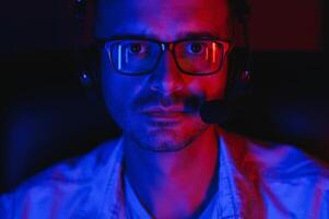Professional Gamer Plays Game on His Computer. He's Participating in Online Cyber Games Tournament or in Internet Cafe. He Wears Glasses and Talks into Microphone. photo
