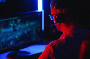 Professional Gamer Plays Game on His Computer. He's Participating in Online Cyber Games Tournament or in Internet Cafe. He Wears Glasses and Talks into Microphone. photo
