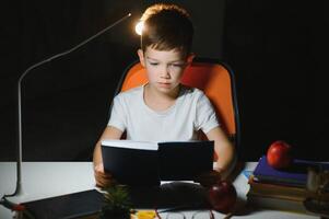 Boy learn lessons in the home setting at the table in the light of a table lamp. photo