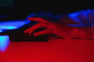 Close-up On Gamer's Hands on a keyboard, Actively Pushing Buttons, Playing MMO Games Online. Background is Lit with Neon Lights. photo