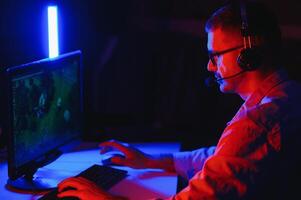 Professional Gamer Plays Game on His Computer. He's Participating in Online Cyber Games Tournament or in Internet Cafe. He Wears Glasses and Talks into Microphone. photo