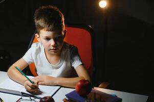 Boy learn lessons in the home setting at the table in the light of a table lamp. photo