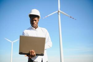 African Engineer standing and hoding laptop with wind turbine photo