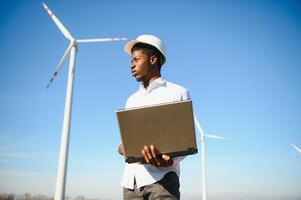 African Engineer standing and hoding laptop with wind turbine photo