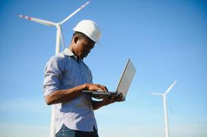 African Engineer standing and hoding laptop with wind turbine photo