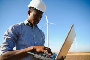 African Engineer standing and hoding laptop with wind turbine photo