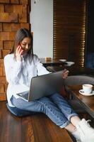 Young woman successful manager is talking via mobile phone with possible financial company employee and reading their resume on portable laptop computer during remote interview in co-working space photo