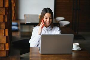 Young woman successful manager is talking via mobile phone with possible financial company employee and reading their resume on portable laptop computer during remote interview in co-working space photo