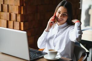 Young woman successful manager is talking via mobile phone with possible financial company employee and reading their resume on portable laptop computer during remote interview in co-working space photo