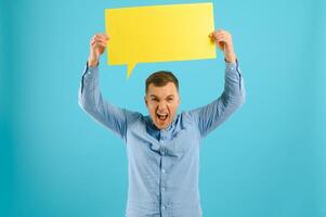 Handsome smiling man holding blank speech bubble sign isolated on light blue studio banner background with copy space photo