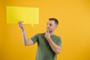 Happy guy smiling and holding blank speech balloon near head against yellow background photo