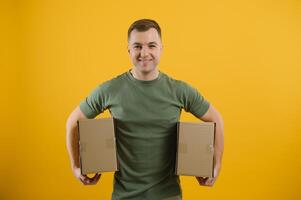 Cute man holding a cardboard box on a yellow background. Delivery service concept. Free space for advertising. photo