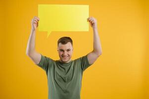 Cheerful young male pointing up and holding empty speech bubble with blank space for quote against vivid yellow background photo