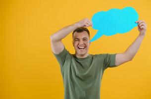 Cheerful young male pointing up and holding empty speech bubble with blank space for quote against vivid yellow background photo