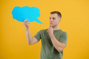 Cheerful young male pointing up and holding empty speech bubble with blank space for quote against vivid yellow background photo