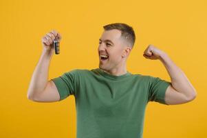 Shocked young man posing isolated on yellow orange background, studio portrait. People emotions lifestyle concept. Mock up copy space. Holding in hand car keys, showing thumb up photo