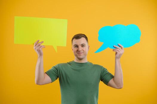 Portrait of cheerful smiling young handsome man holding and looking up at speech bubble with empty space for text on colorful yellow studio background photo