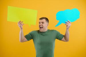Portrait of cheerful smiling young handsome man holding and looking up at speech bubble with empty space for text on colorful yellow studio background photo