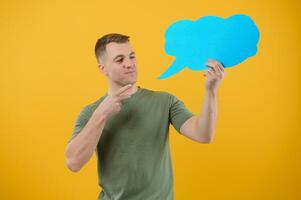Handsome man holding blank speech bubble sign isolated on yellow studio background photo