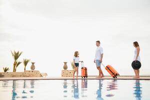 young family with suitcases walking to hotel building with beautiful swimming pool. traveling and relaxing time concept. photo
