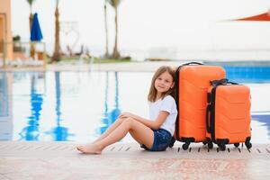 Girl with suitcases by the pool in a luxury hotel. sea and reflection, traveling and relaxing time concept. photo