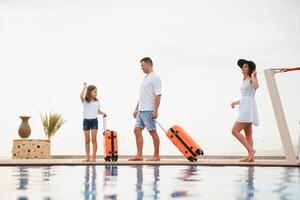 young family with suitcases walking to hotel building with beautiful swimming pool. traveling and relaxing time concept. photo