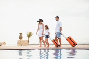 young family with suitcases walking to hotel building with beautiful swimming pool. traveling and relaxing time concept. photo