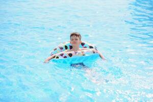 Happy boy in swimming pool. Boy is alone, swimming inflatable ring and surronded by water splashes. Wet teenager is enjoying summer weekend in amusement water park. Banner with copy space photo