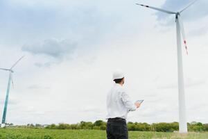 Engineer is checking energy production on wind turbine. Worker in windmills park in helmet and with tablet. photo