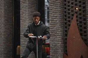 Active Leisure Concept. Side view of black male student driving stand-up scooter over brick road, copy space for ad or text photo