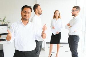 Portrait of smiling indian businessman standing in modern office on colleagues background photo