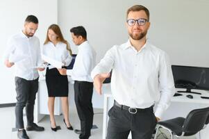 Portrait Of Young Handsome Businessman In Office With Colleagues in The Background photo