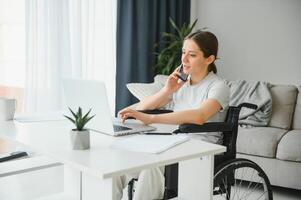 Female freelance programmer sitting in wheelchair and using computers while coding web game at home. photo