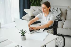 Freelancer in wheelchair using laptop near notebook and papers on table photo