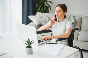 Freelancer in wheelchair using laptop near notebook and papers on table photo