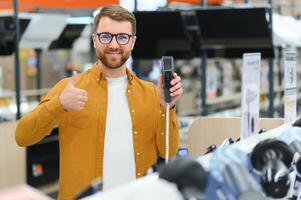 A bearded stylish man makes a choice while standing at a showcase with electronic trimmers and razors photo