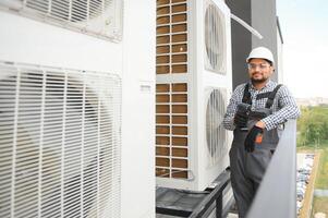 Indian Repairman in uniform installing the outside unit of air conditioner photo