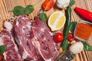 Raw pork meat with spices and vegetables on wooden table. photo