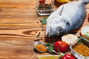 Fresh raw dorado fish. Sea bream, lying on a wooden board on a table with herbs and salt and spices. Dorado and ingredients for cooking on the table. Close-up. photo