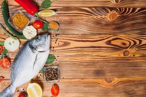 Fresh raw dorado fish on baking paper with lemon, pepper, tomatoes and various spices on wooden background with copy space photo