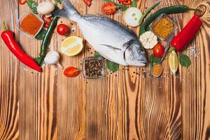 Fresh raw dorado fish on baking paper with lemon, pepper, tomatoes and various spices on wooden background with copy space photo