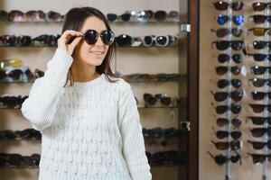 She made her choice. Beautiful young woman adjusting her new sunglasses and smiling while standing in optic store. photo