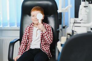 Child at eye sight test. Little kid selecting glasses at optician store. Eyesight measurement for school kids. Eye wear for children. Doctor performing eye check. Boy with spectacles at letter chart photo