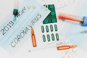 a test tube with a positive test for the CAVID-2019 coronavirus. medical devices on a white table. thermometer, phonendoscope, tablets, surgical masks photo