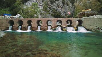Drone captures bridge over rocky mountain stream. Clear water flows under bridge in scenic setting. Aerial view highlights bridge crossing fast stream video